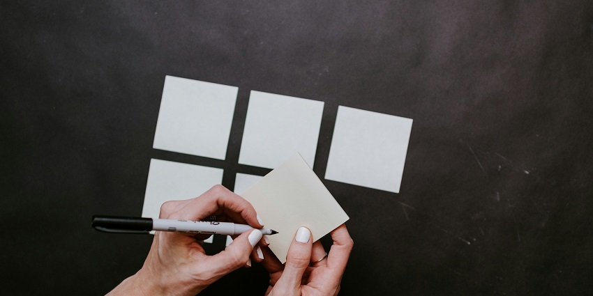 A view of a person’s hand holding a black pen and writing on a white piece of paper.