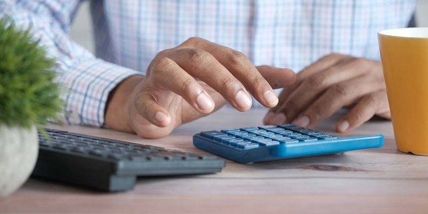 A frontal view of a man wearing a blue shirt using a black calculator on a table.