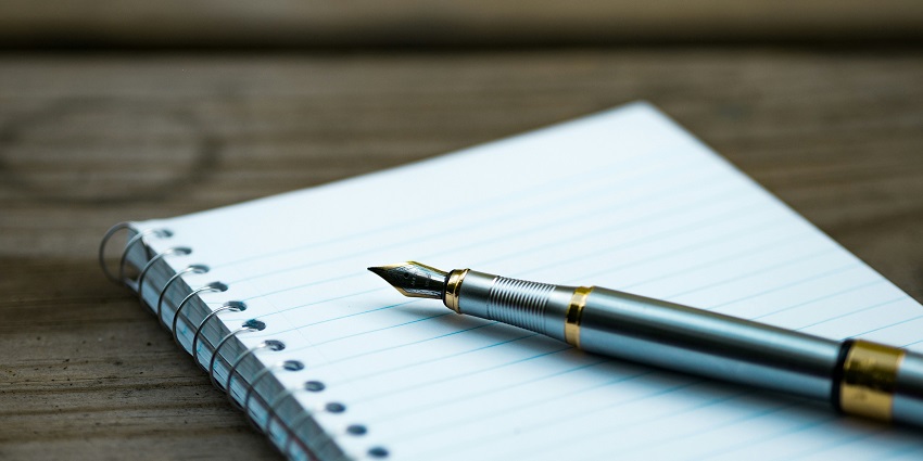 A side view of a white notebook with a fountain pen on top of it kept on a table.