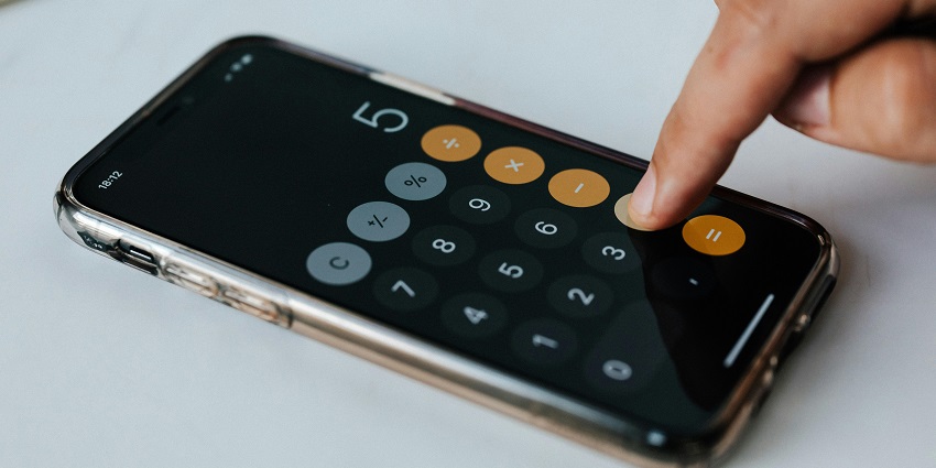 A selectively focused side view of a person using a calculator sitting on a white table.