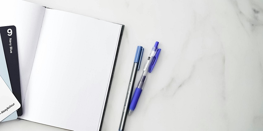 An aerial shot of a white paper with different pens sitting on it kept on a table.