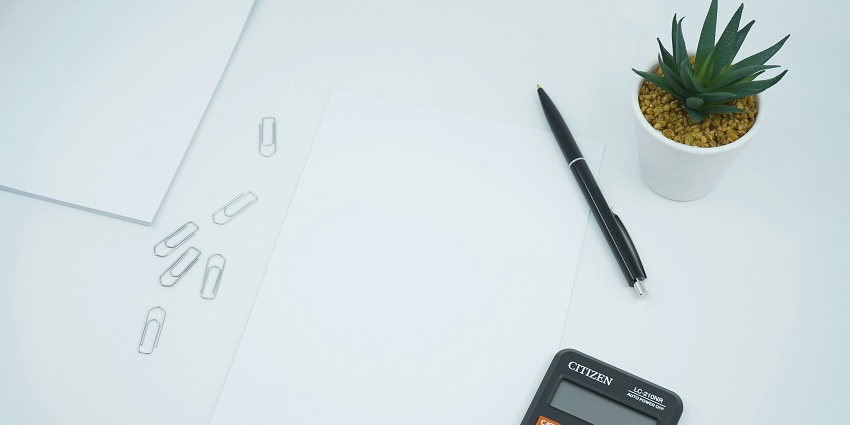 A view of a black calculator on a table on the side of a white paper with a pen.
