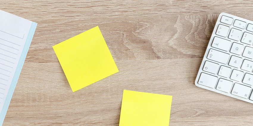 An aerial view of sticky yellow notes on a table with a keyboard and a notebook.