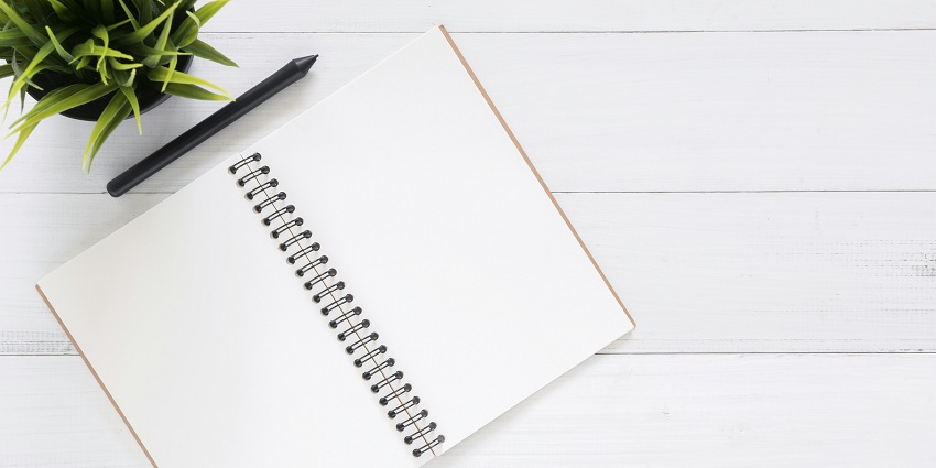 A view of a blank white open notebook from above with a pen and leaves on the side.
