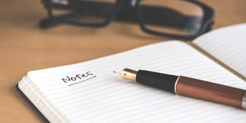 A view of an open notebook with the word notes written on it and a brown fountain pen.