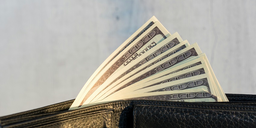A view of a black wallet with a lot of money sticking out of it during the daytime.