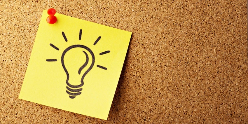 A focused view of a yellow sticky note with a red bulb drawn on it with a push pin.