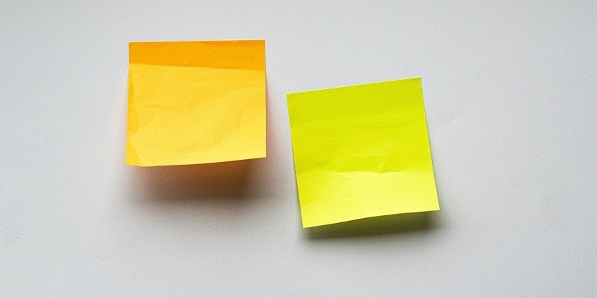 A frontal view of two yellow and green sticky notes placed on a plain white surface.