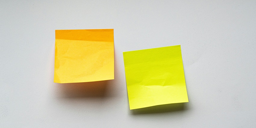 A selectively focused view of yellow and green sticky notes on a plain white surface.