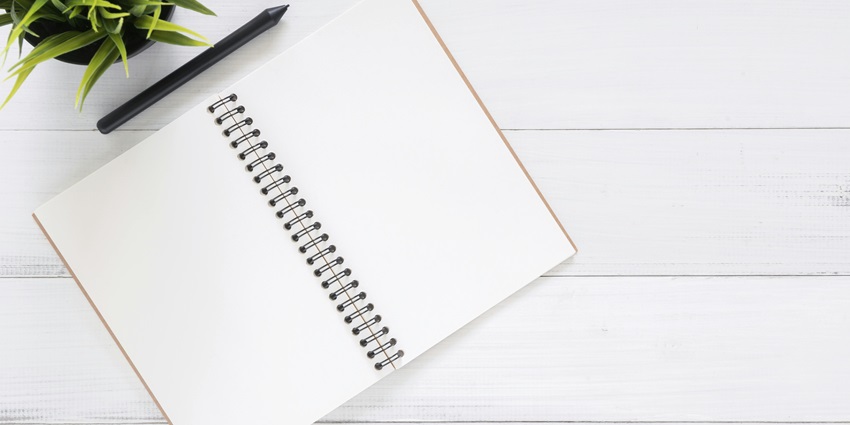 An aerial view of a white notebook with a black pen and a green plant on the side.