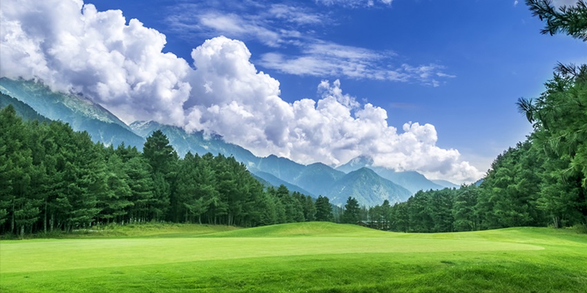 Picturesque view of Pahalgam Gold Course surrounded by lush greenery under clear blue sky and white clouds