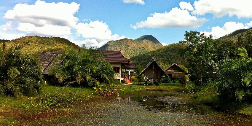 A scenic view of a small accommodation surrounded by lush hills and Palm trees in Thailand