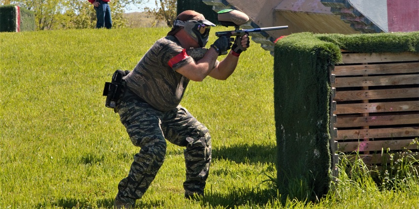 A picture of a person wearing protective gear and aiming at opponents in a paintball game
