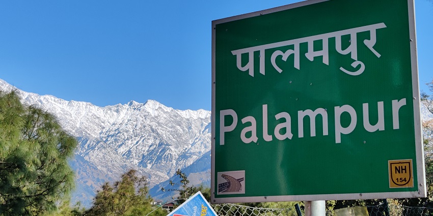Sign displaying the name "Palampur" against a scenic backdrop of hills and greenery.