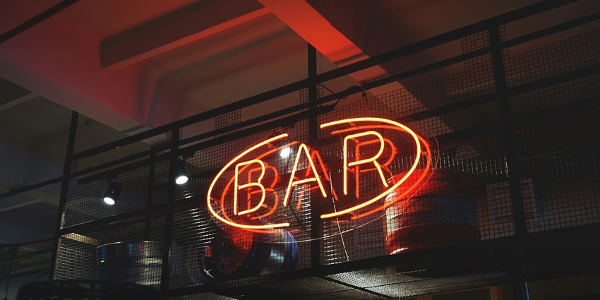 Image of a bar with a sign written BAR with colourful red lights behind dark background
