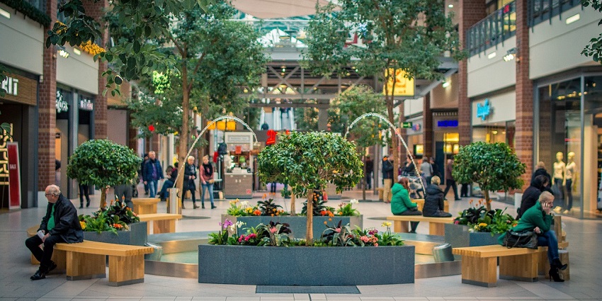 A picture of people sitting on brown wooden benches with plants in the surroundings.