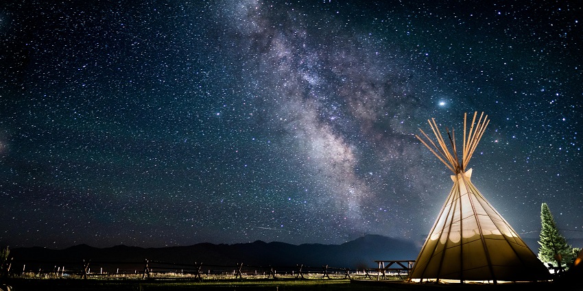 A stunning view of a tent under the canopy of the stars around lush green meadows.