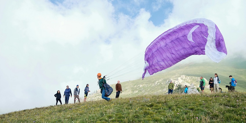 People watching a paraglider take off from a grassy field with a colorful parachute.