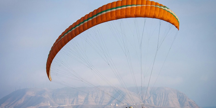 Several paragliders resting on green grass with colorful canopies, ready for takeoff.
