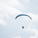 A mesmerising view of a person in the sky with a paragliding parachute during the daytime.