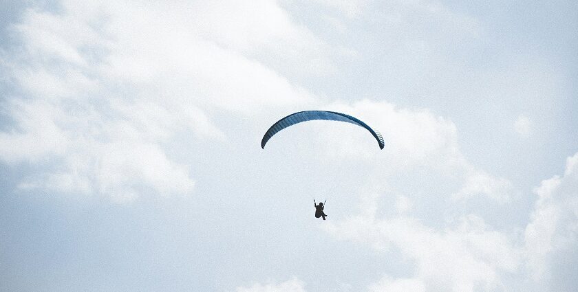 A mesmerising view of a person in the sky with a paragliding parachute during the daytime.