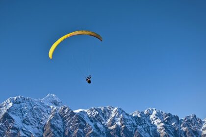 A scenic view of a person soaring high above in the air over the snow-capped peaks.