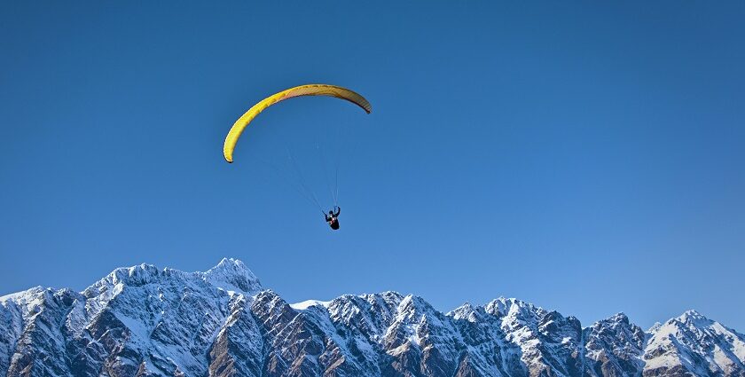 A scenic view of a person soaring high above in the air over the snow-capped peaks.