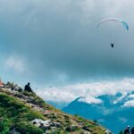 A breathtaking aerial view of a person enjoying Paragliding in the clear blue skies.