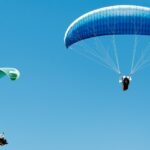 A breathtaking view of two people enjoying paragliding across the clear blue skies.