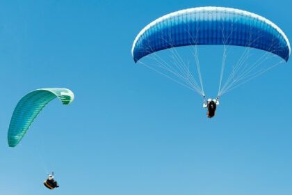 A breathtaking view of two people enjoying paragliding across the clear blue skies.