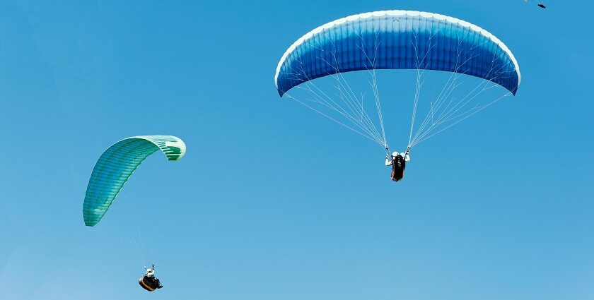 A breathtaking view of two people enjoying paragliding across the clear blue skies.