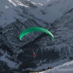 A stunning view of a person paragliding in front of snow-capped mountains during the day.