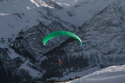 A stunning view of a person paragliding in front of snow-capped mountains during the day.