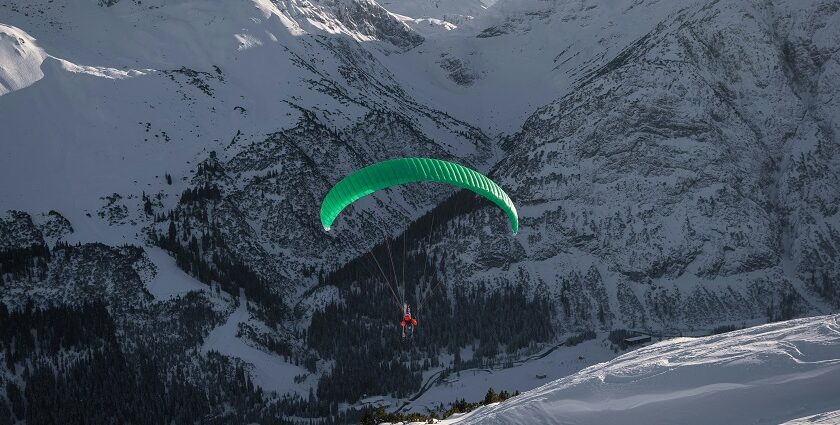 A stunning view of a person paragliding in front of snow-capped mountains during the day.