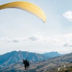 A scenic view of a person soaring high up in the sky amidst the green-capped peaks.