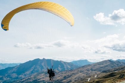 A scenic view of a person soaring high up in the sky amidst the green-capped peaks.