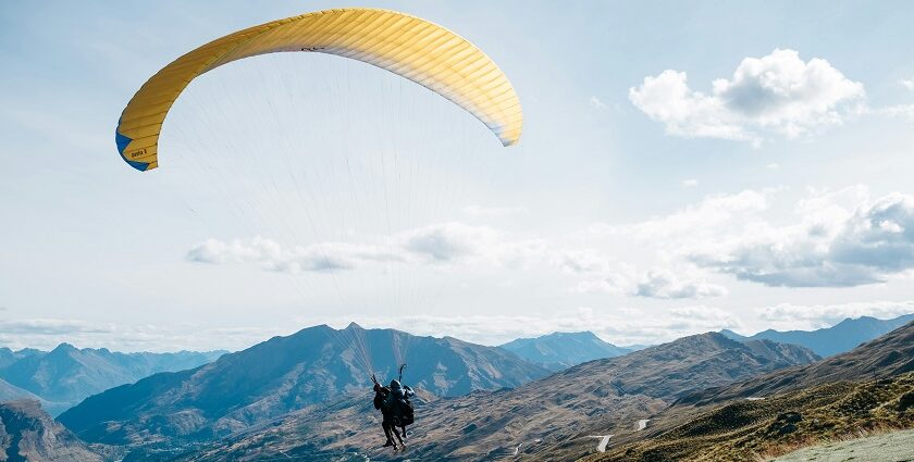 A scenic view of a person soaring high up in the sky amidst the green-capped peaks.