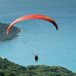 Person paragliding high above a dense forest with a colorful parachute - paragliding in Shillong.