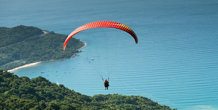 Person paragliding high above a dense forest with a colorful parachute - paragliding in Shillong.