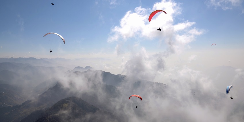 Image of a paraglider soaring over lush green hills - Hill stations near Kangra.