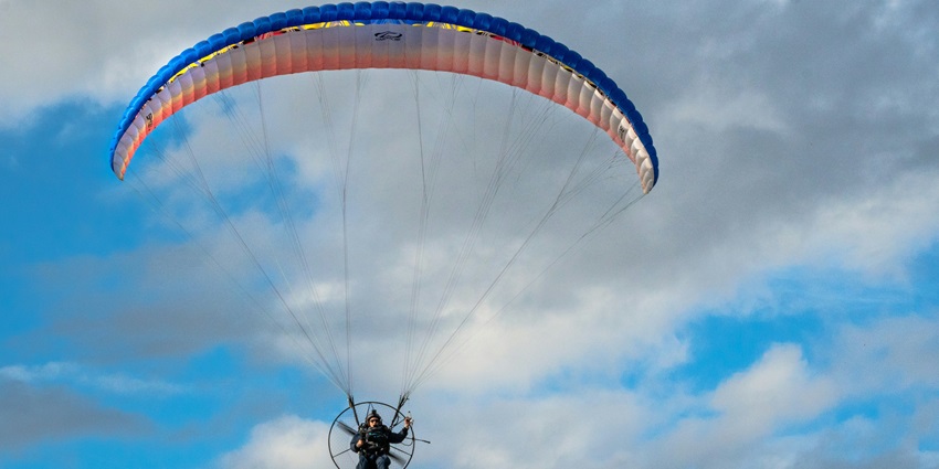 Person parasailing with a colourful parachute against a cloudy sky backdrop