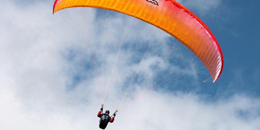 Person suspended beneath a vibrant orange parachute against a blue, cloudy sky