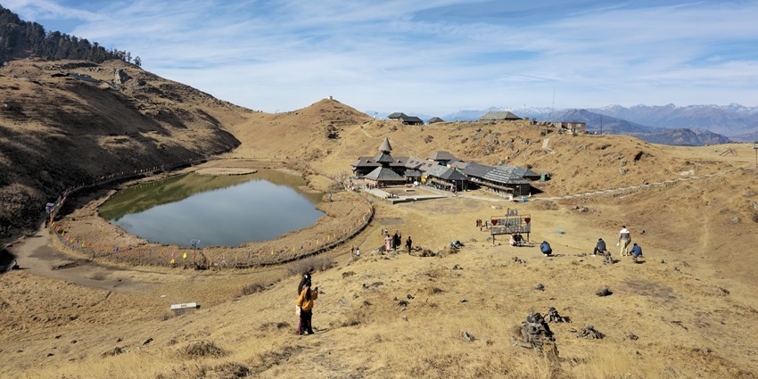 A panoramic picture of a lake with a temple nearby and mountains in the background