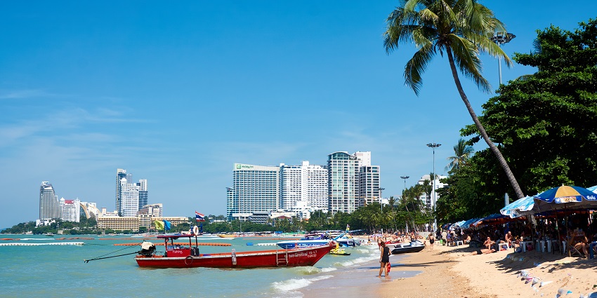 Different types of boats and ferries at the shore of Pattaya beach with the cityscape in the background
