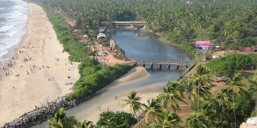 An aerial picture of a beach in Kerala with pine trees and a canal on the other side of the sand