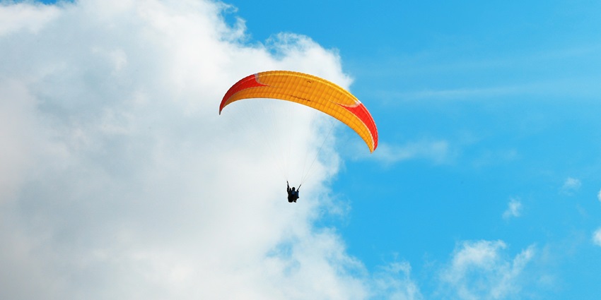 Riding a parachute, soaring high above scenic landscapes with panoramic views below.