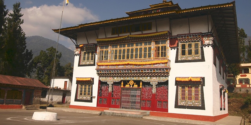 A frontal view of a traditional monastery in Sikkim, surrounded by lush green gardens and rolling hills