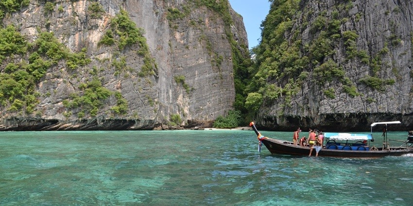 A picture of people in a boat sailing in turquoise waters of Phuket with tall rocky islands in the background