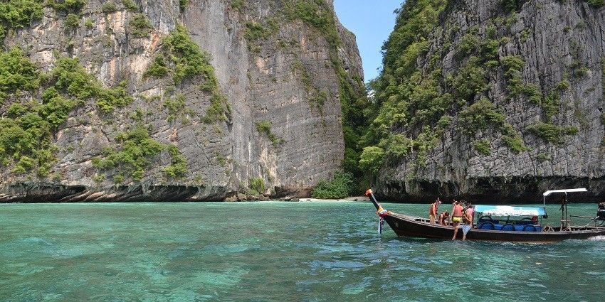 A picture of a boat sailing in clear waters in Thailand with an island in background