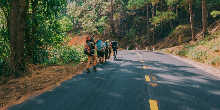 Group of people walking beside the road, exploring the landscape outdoor on hiking.
